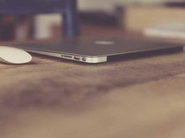 Kompjuter macbook air ngjyre gri dhe nje mouse i bardhe mbi nje tavoline druri