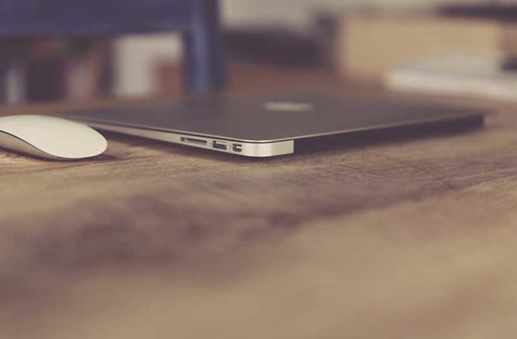 Kompjuter macbook air ngjyre gri dhe nje mouse i bardhe mbi nje tavoline druri